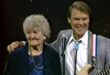 Glen Campbell with his arm around his mother Carrie as they sing together on stage