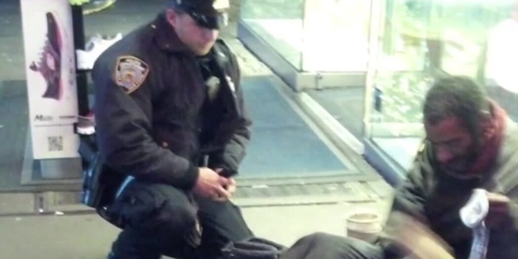 NYPD Officer Larry DePrimo kneeling beside a barefoot man in Times Square in November 2012
