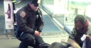 NYPD Officer Larry DePrimo kneeling beside a barefoot man in Times Square in November 2012