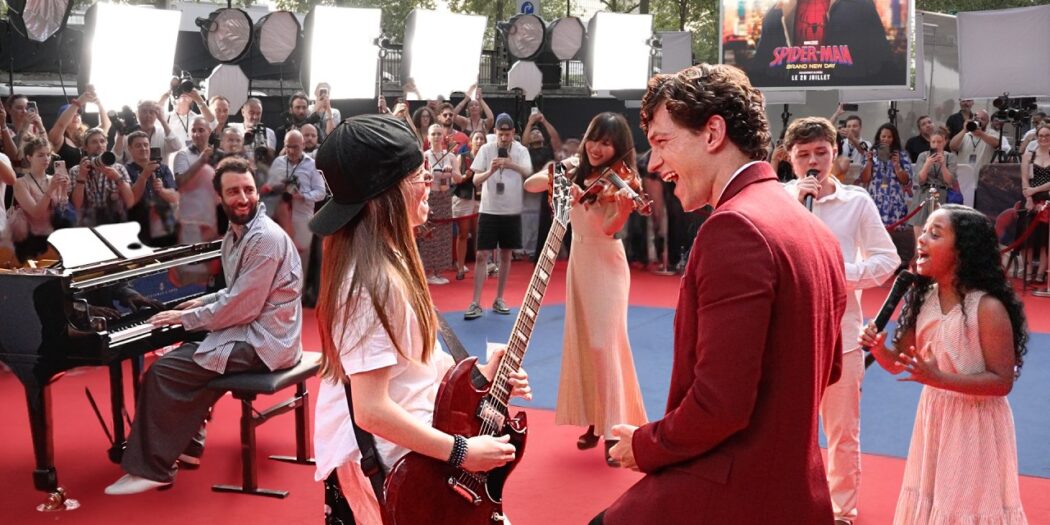 Tom Holland kneeling beside a little girl holding a microphone at a Spider-Man fan event in Paris