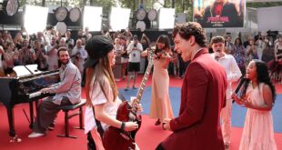 Tom Holland kneeling beside a little girl holding a microphone at a Spider-Man fan event in Paris